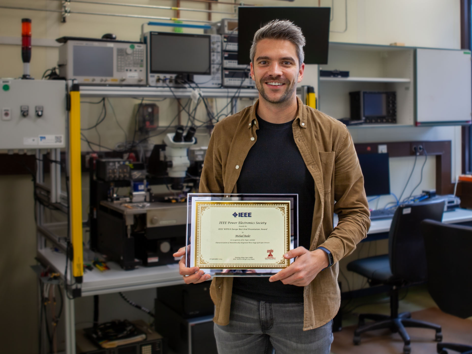 Michael Basler hält die Urkunde seines Awards in einem Labor des Fraunhofer IAF