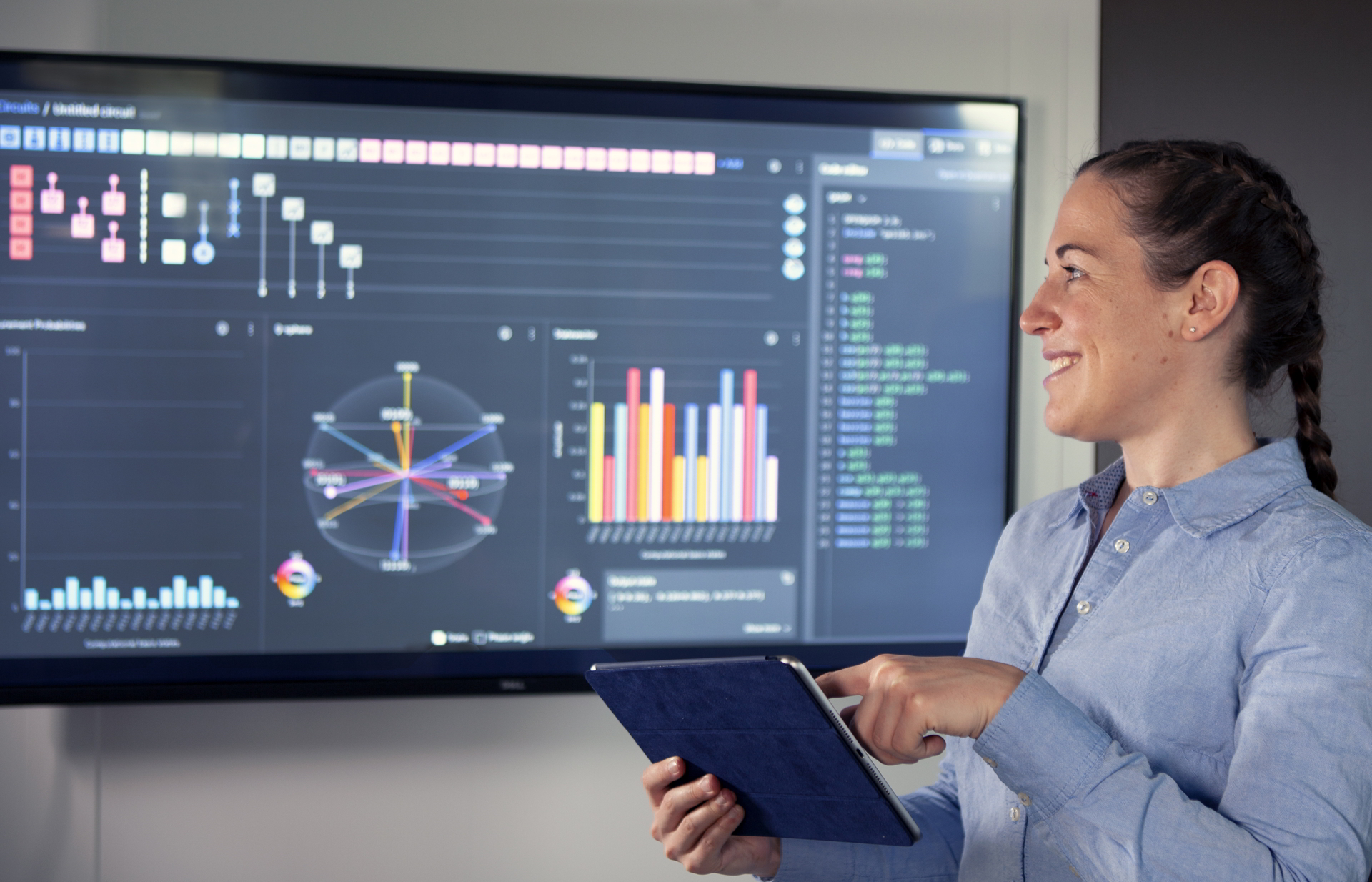 Young woman operates a tablet and looks at a monitor of the Qiskit user interface.